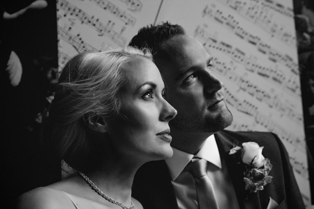 Black and white close-up of bride and groom looking upward with musical notes in background, Umbria wedding photographer style