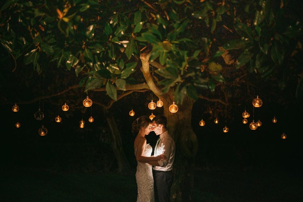 Bride and groom under a tree with hanging lanterns at night, in a magical scene captured by a Puglia wedding photographer