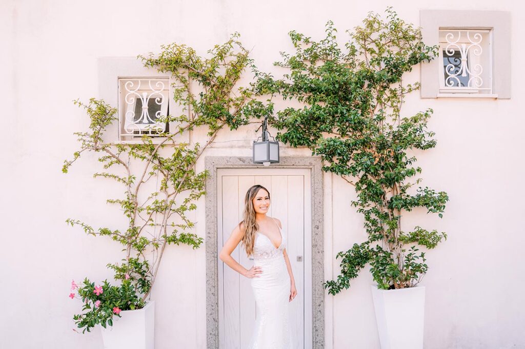 Smiling bride posing in front of a pastel villa facade with green vines, captured by a Puglia wedding photographer