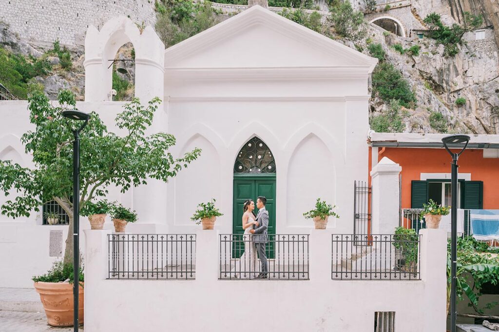 Wedding couple embracing in front of a white church with green doors and Mediterranean details, captured by a Puglia wedding photographer