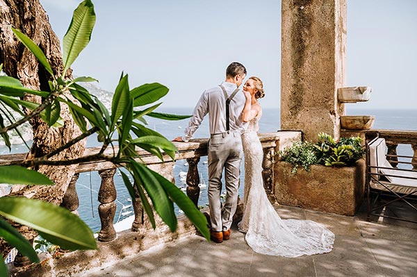 A newlywed couple embracing near a rustic stone wall surrounded by lush greenery, ideal for an Italian wedding