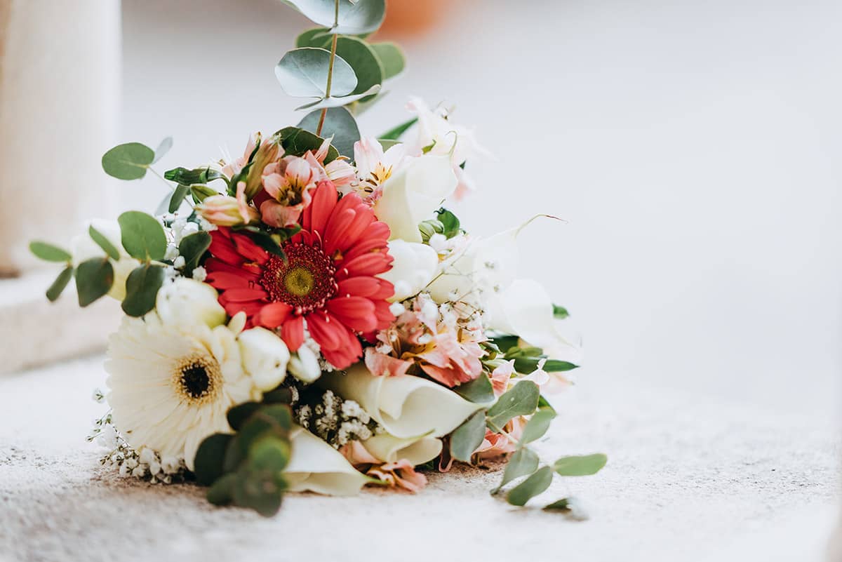 A colorful wedding bouquet with red and white flowers, eucalyptus, and greenery, perfect for a rustic chic wedding in Tuscany