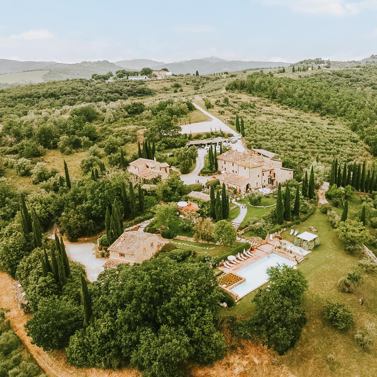 An aerial view of a charming Tuscan estate surrounded by olive groves, cypress trees, and rolling hills, ideal for a budget-friendly wedding venue