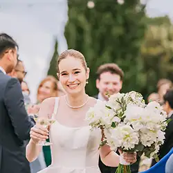 Smiling bride holding a bouquet of white flowers with friends in the background